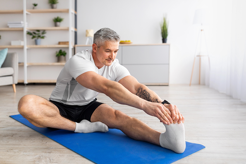 Home workout. Sporty mature man stretching her leg